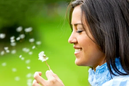 Bella donna che soffia un fiore e sorride
